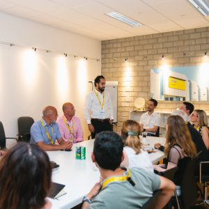 People sitting around a table listening to someone speaking ©ICONIC Digital Agency